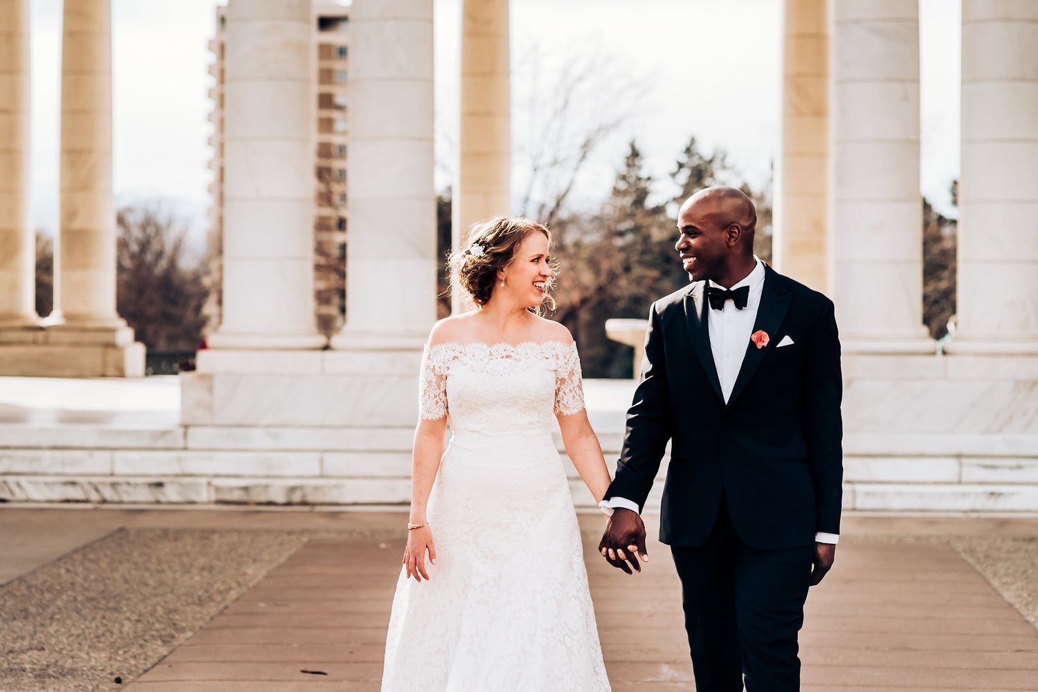 Newlyweds sharing a joyful moment while walking among elegant white columns.
