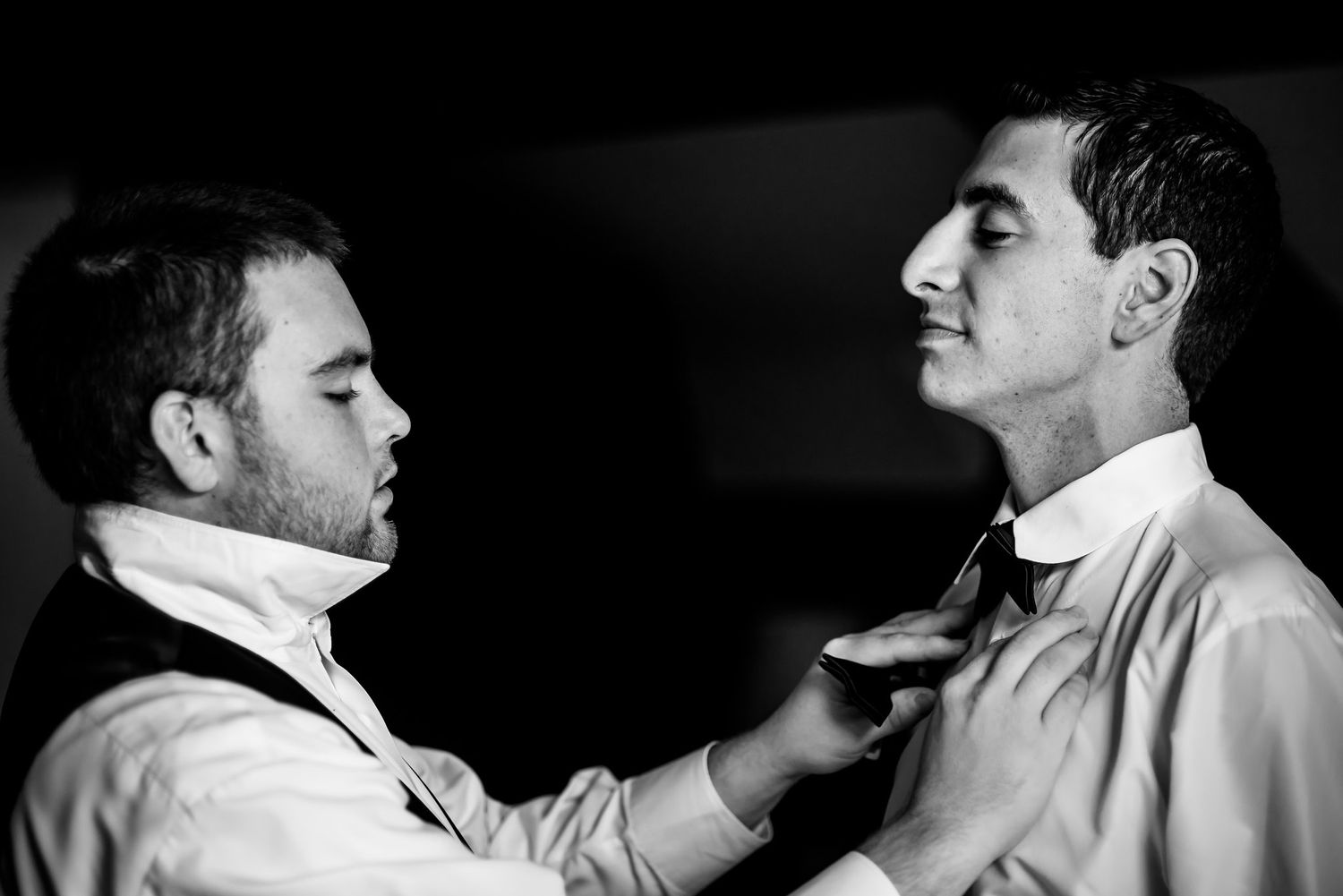 Black and white image of formal wear preparation with bow tie adjustment.