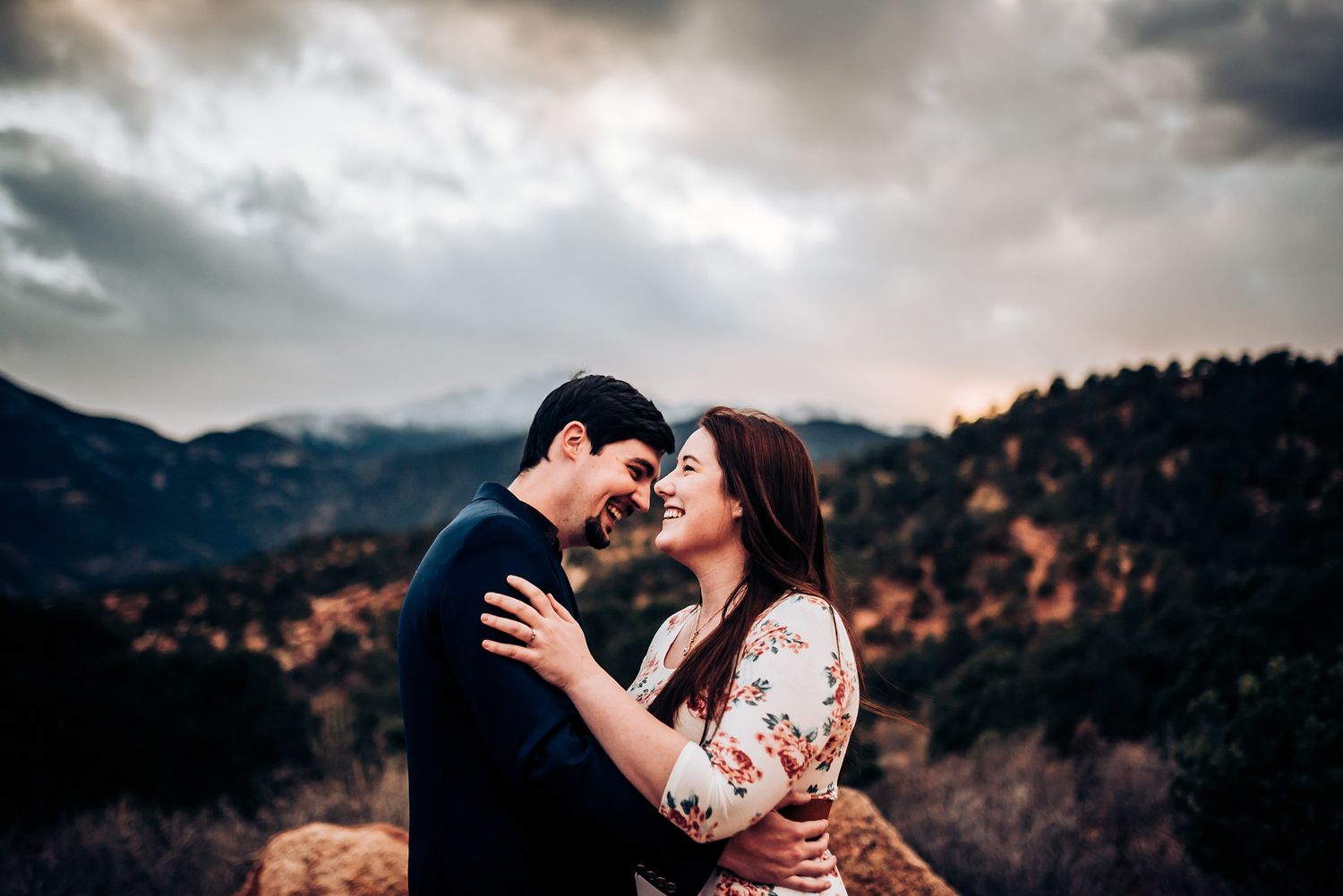 A romantic couple shares an intimate moment against a backdrop of misty mountains at sunset.
