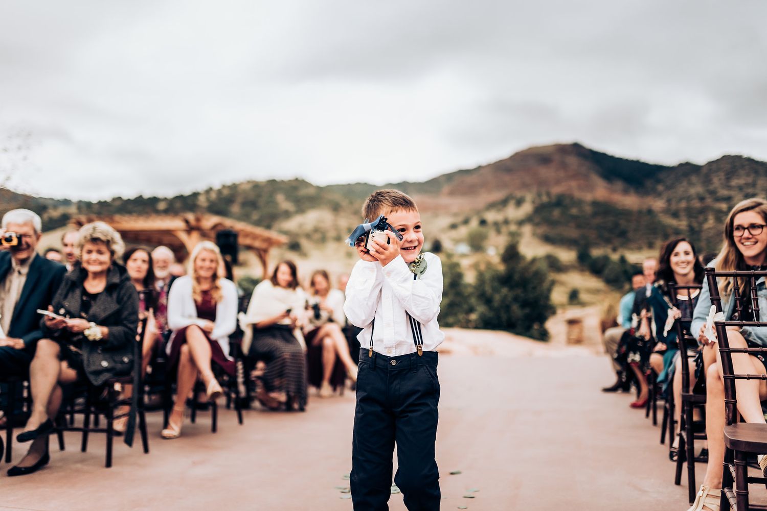 A young ring bearer walks down the aisle at an outdoor wedding ceremony.