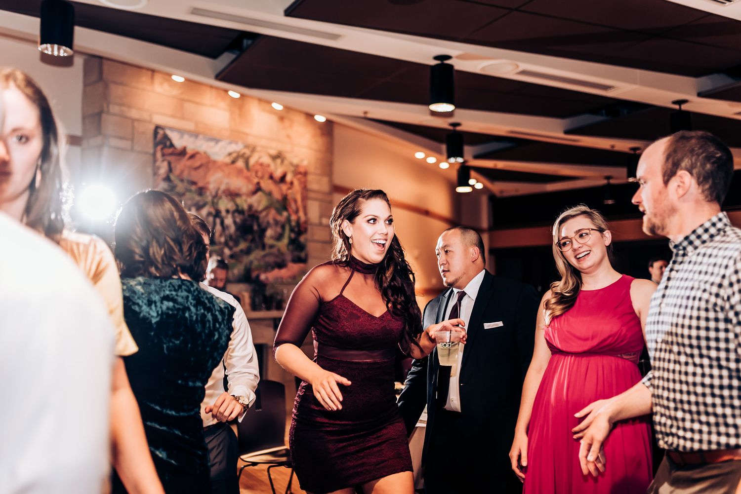 Party guests socializing and dancing in a venue with exposed beam ceiling.