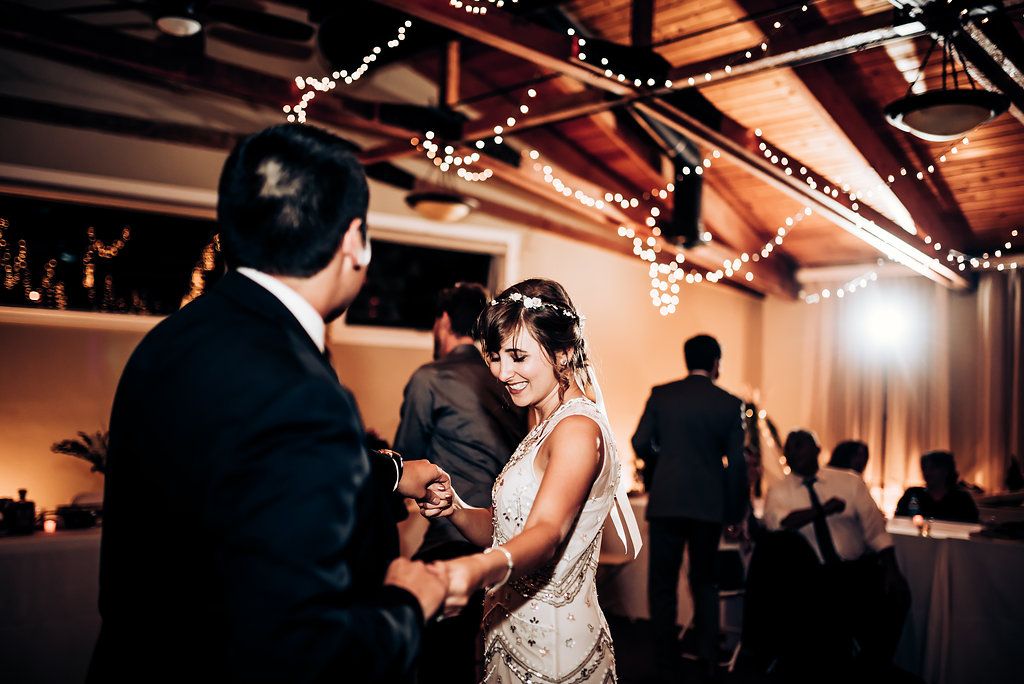 Guests dance together beneath string lights at an elegant indoor wedding reception venue.