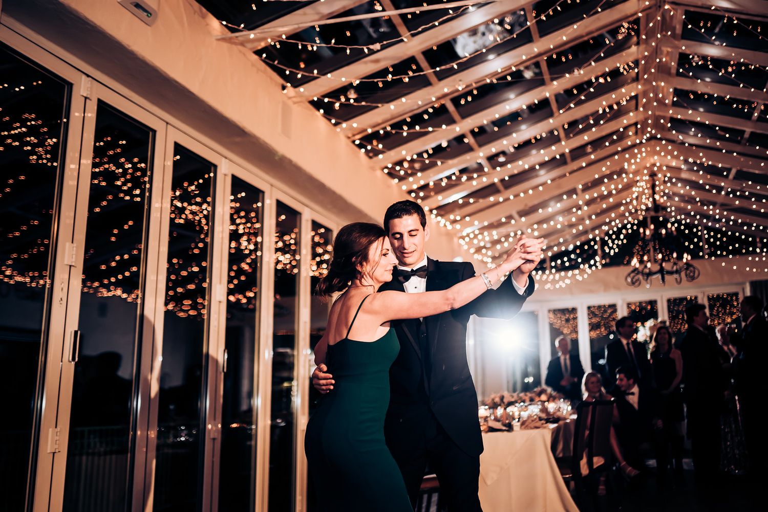 Couple dancing under romantic string light canopy at evening wedding reception.