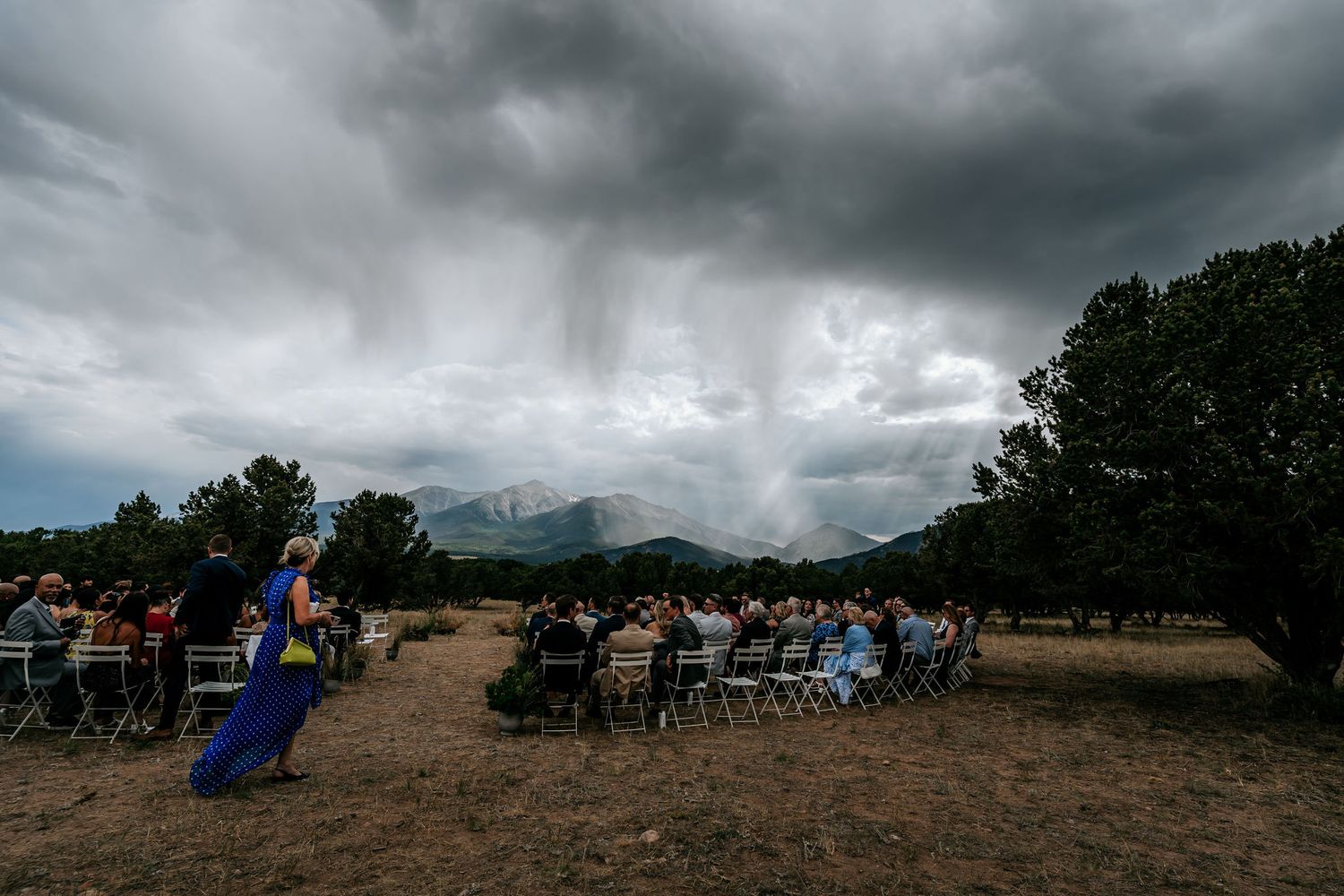 Outdoor wedding ceremony setup with dramatic storm clouds rolling over mountain peaks.