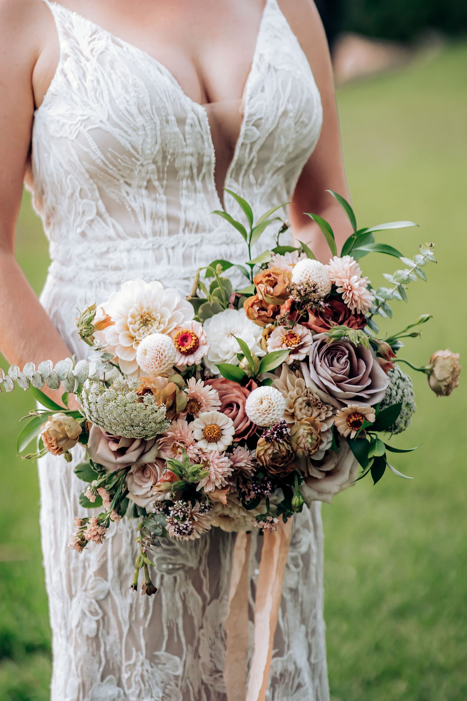 An elegant bridal bouquet with roses and mixed flowers against a detailed lace wedding dress.