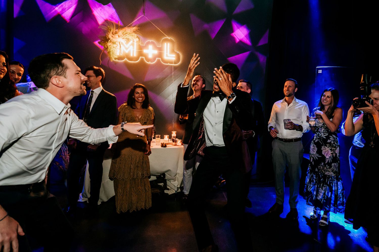 Guests dancing and celebrating with a neon sign glowing in the background.