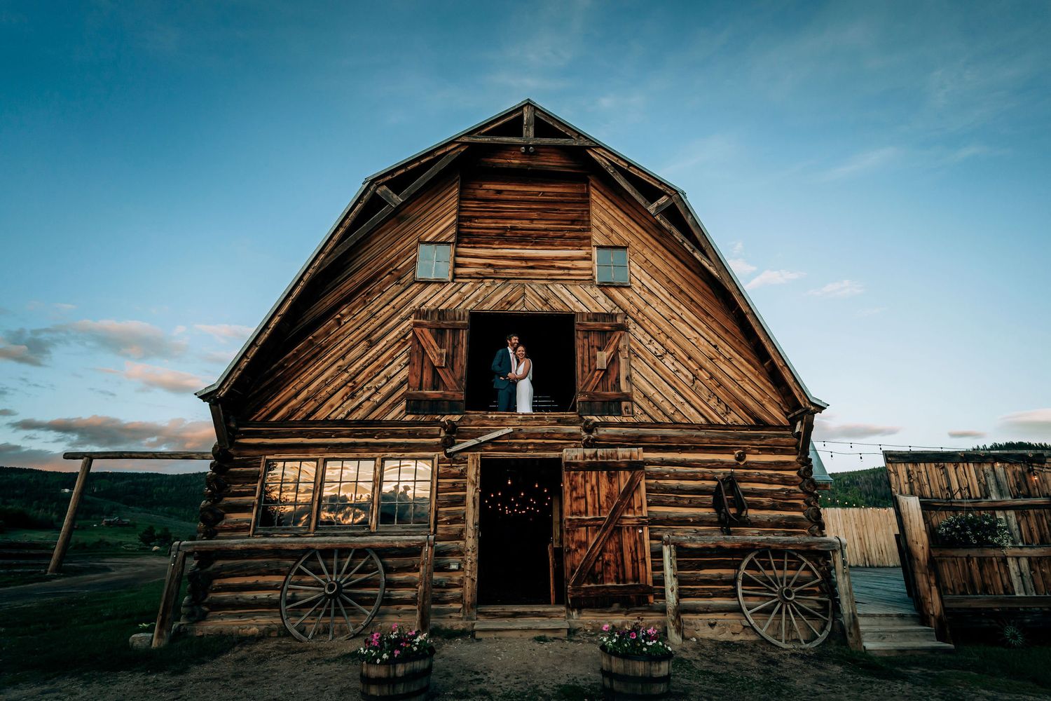 A historic wooden barn with diagonal siding stands against a dusky blue sky.