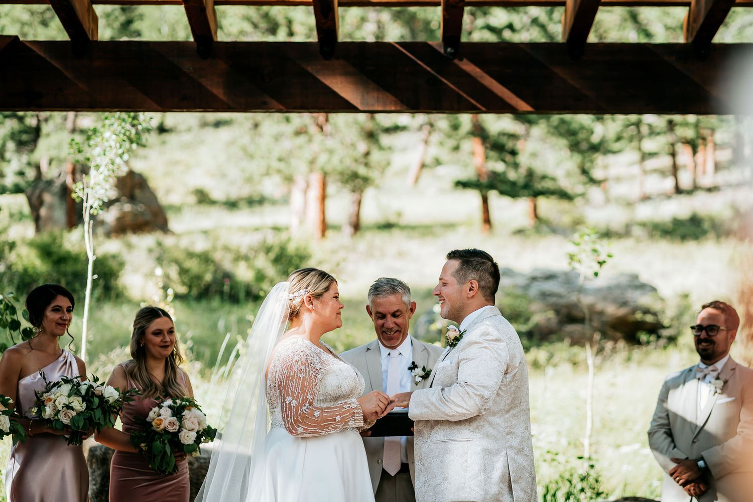 Wedding ceremony taking place under a wooden pergola in a scenic mountain setting.