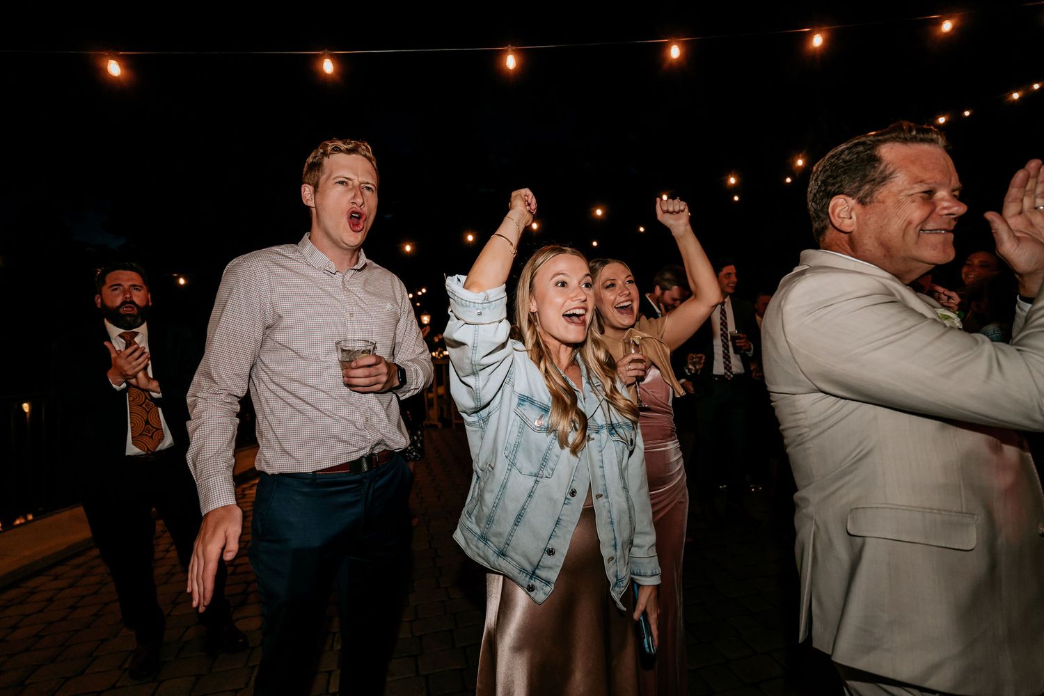 Party guests dancing under string lights at a wedding reception celebration.