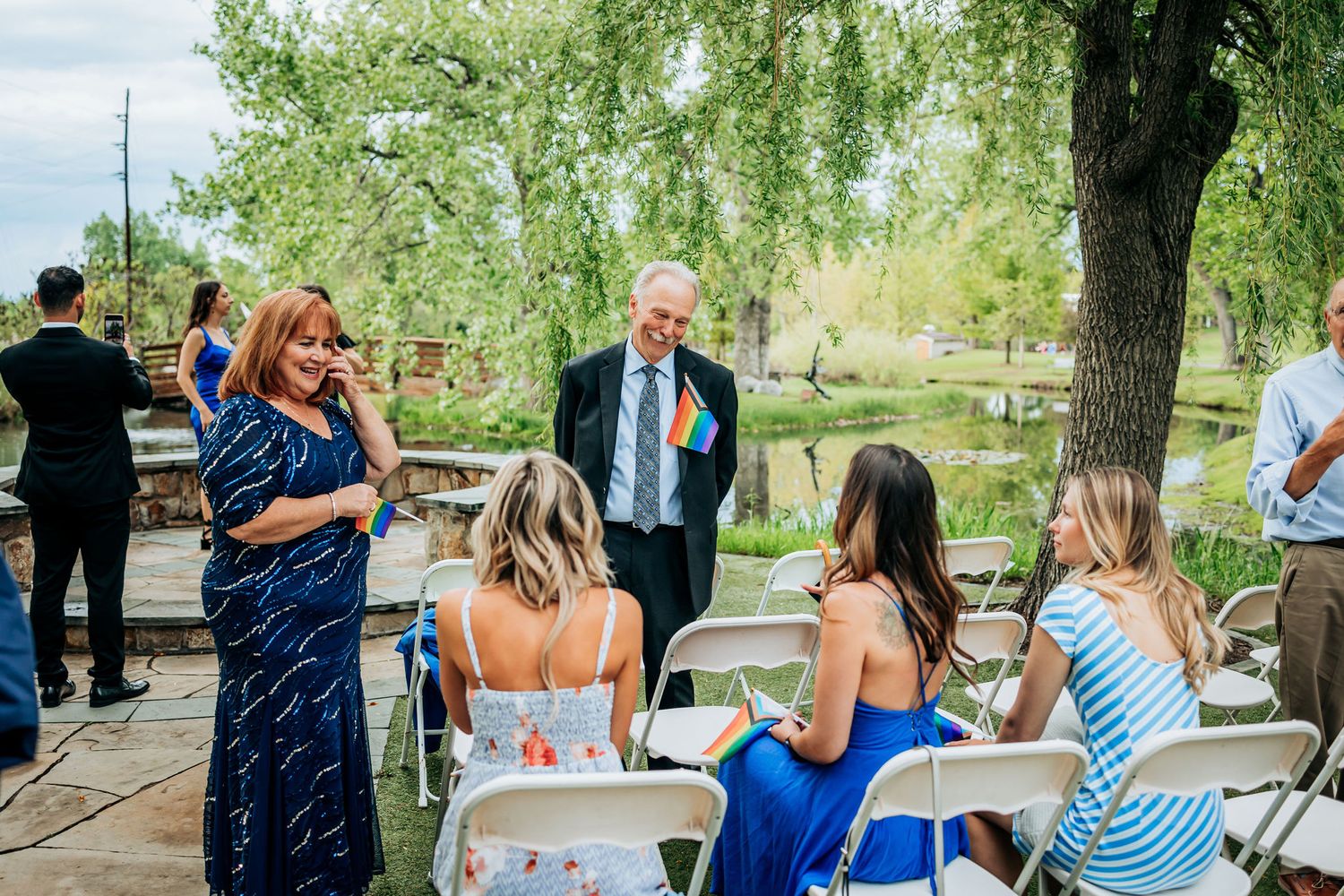 Wedding guests mingling on an outdoor patio with willow trees in the background.