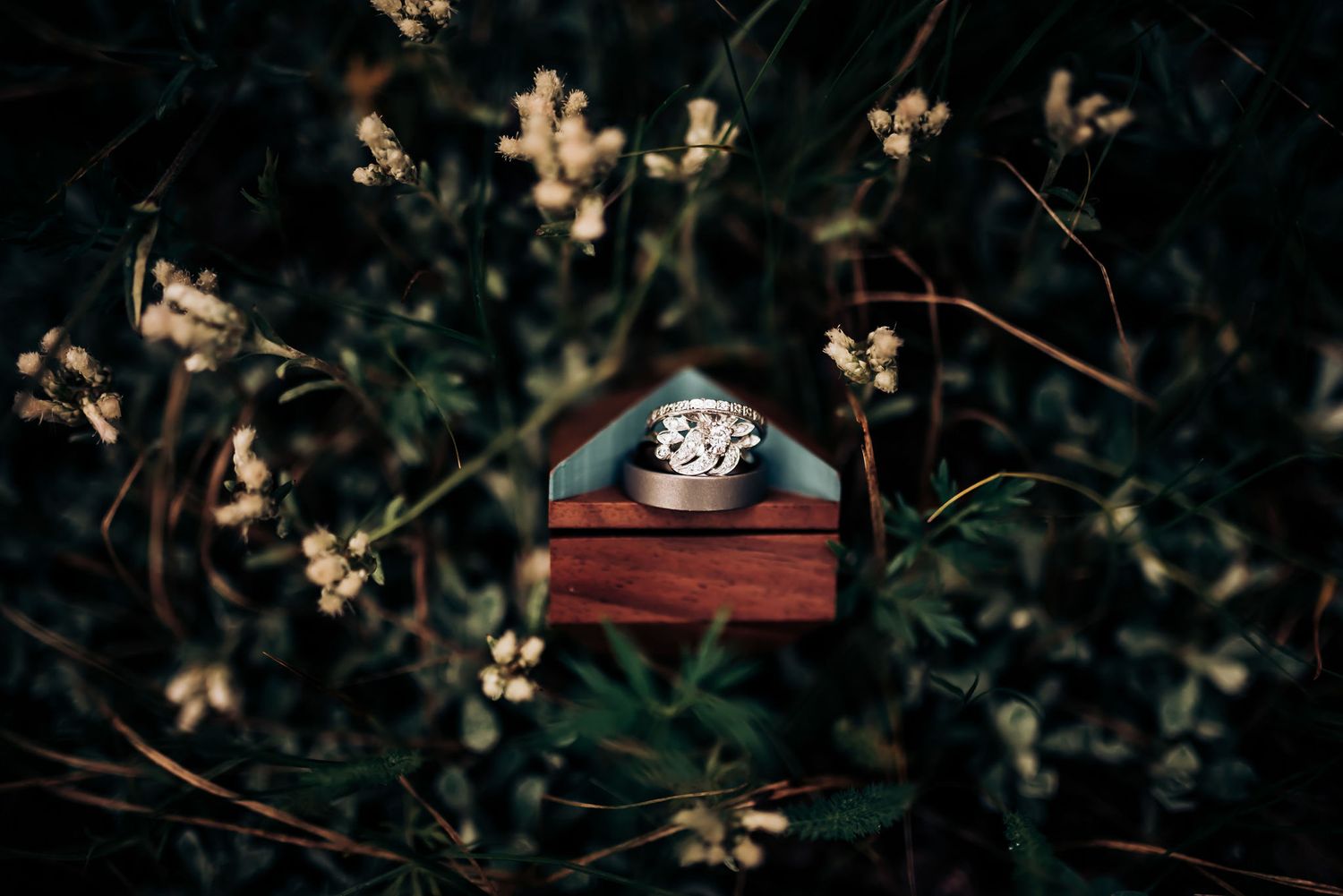 Diamond engagement ring in wooden box surrounded by delicate flowers.