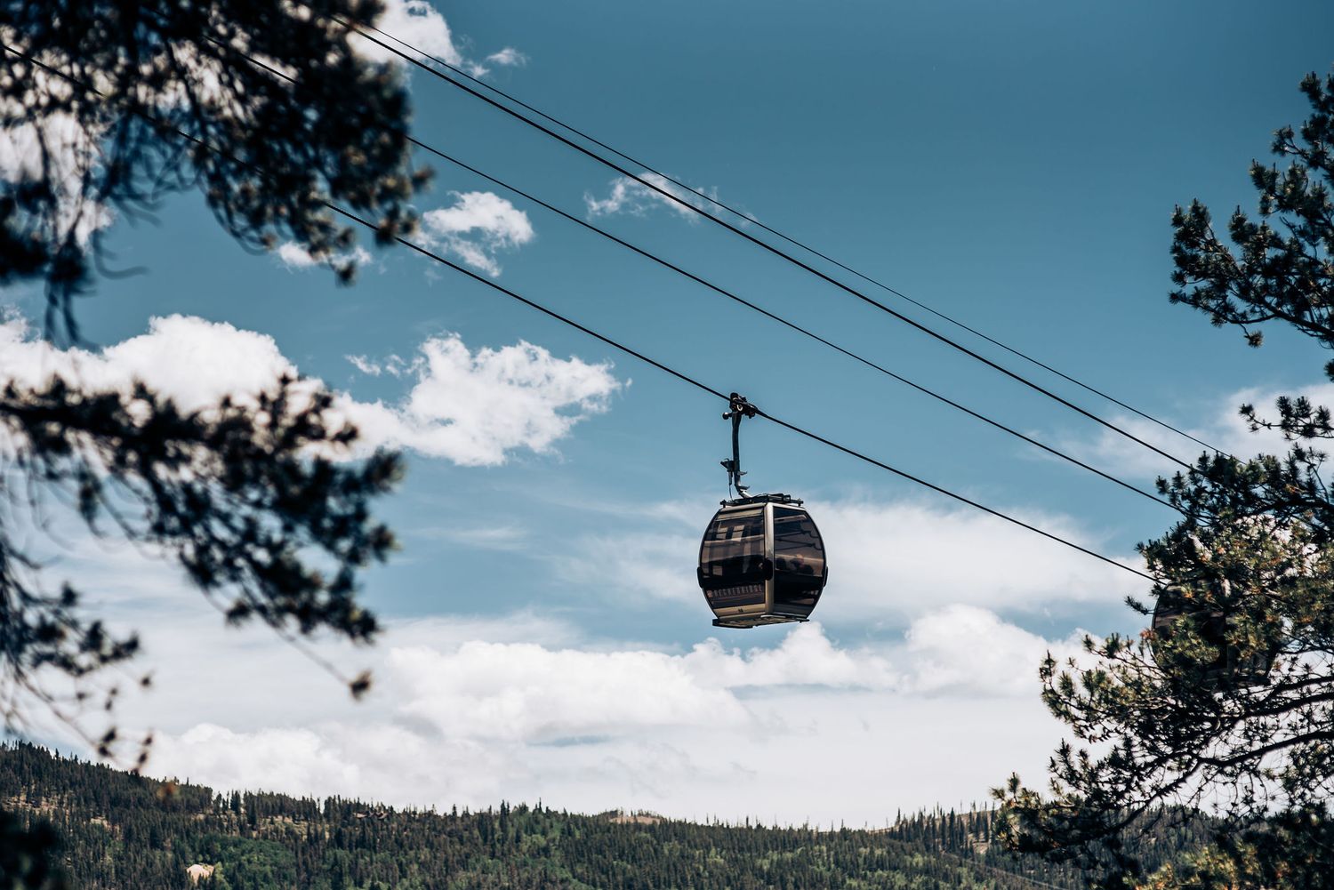 Gondola lift cable car against blue sky with mountain landscape and clouds.