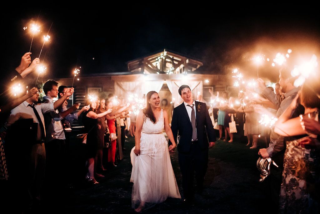 Sparkler exit at nighttime wedding with couple walking through glowing archway of lights.