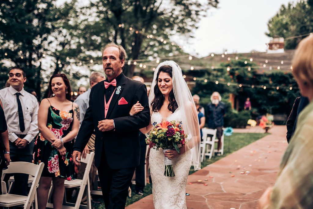 Wedding processional along a brick pathway with guests seated in white chairs.