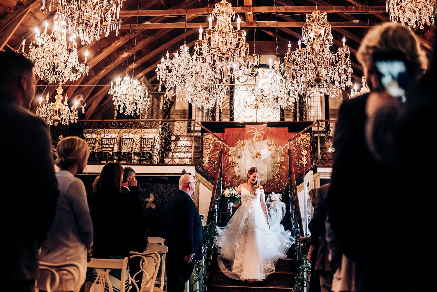 Wedding ceremony in an elegant venue with crystal chandeliers hanging from wooden beams.