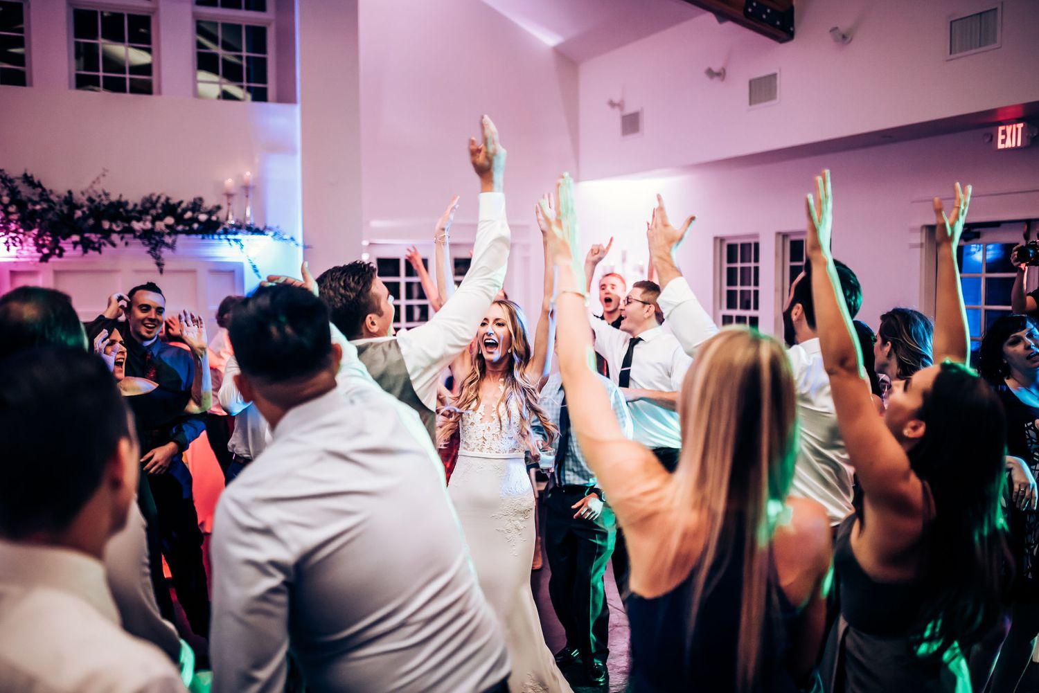 Enthusiastic crowd dancing with hands raised during a wedding celebration.