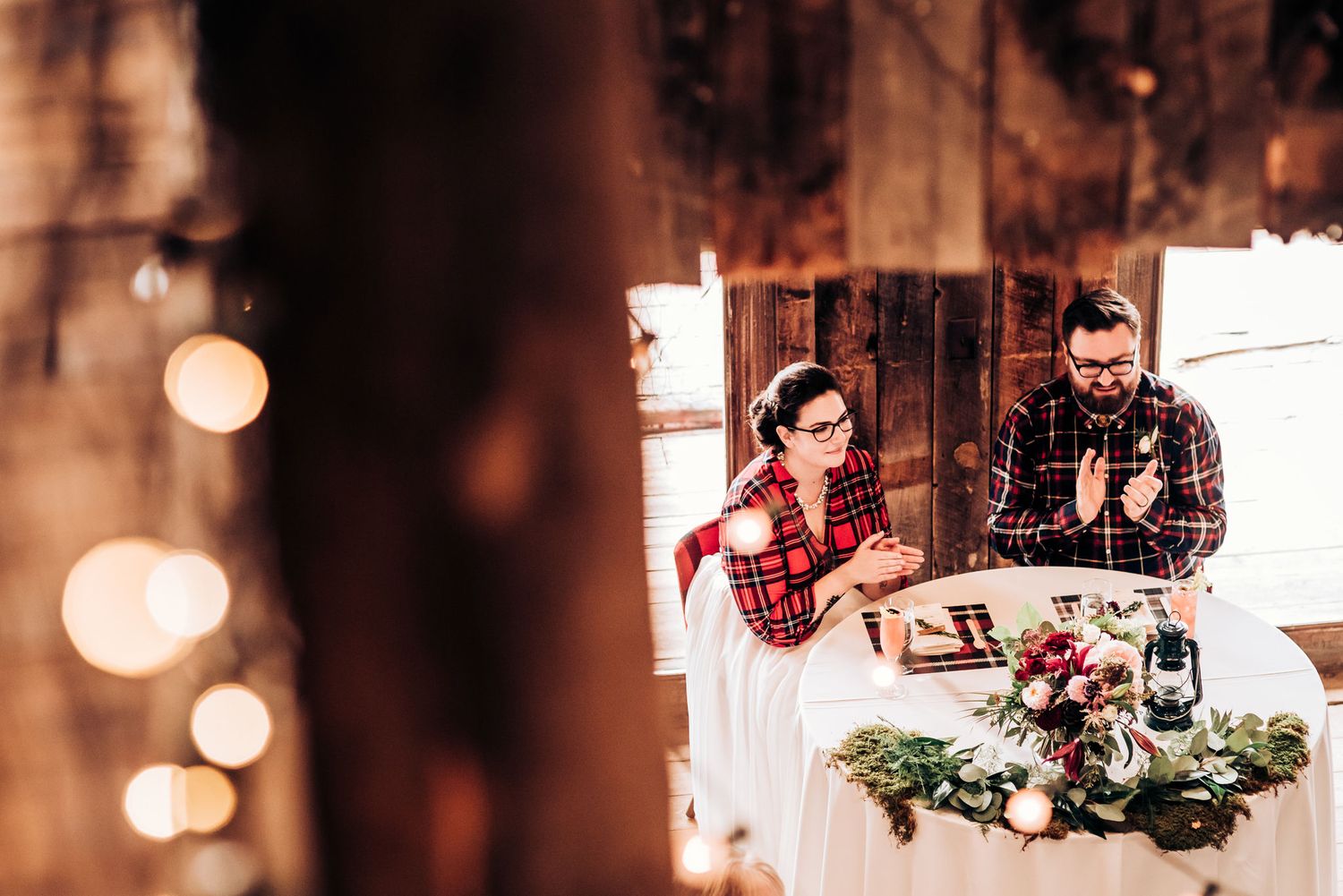 Couple celebrates at rustic wedding reception with lanterns and greenery centerpiece.