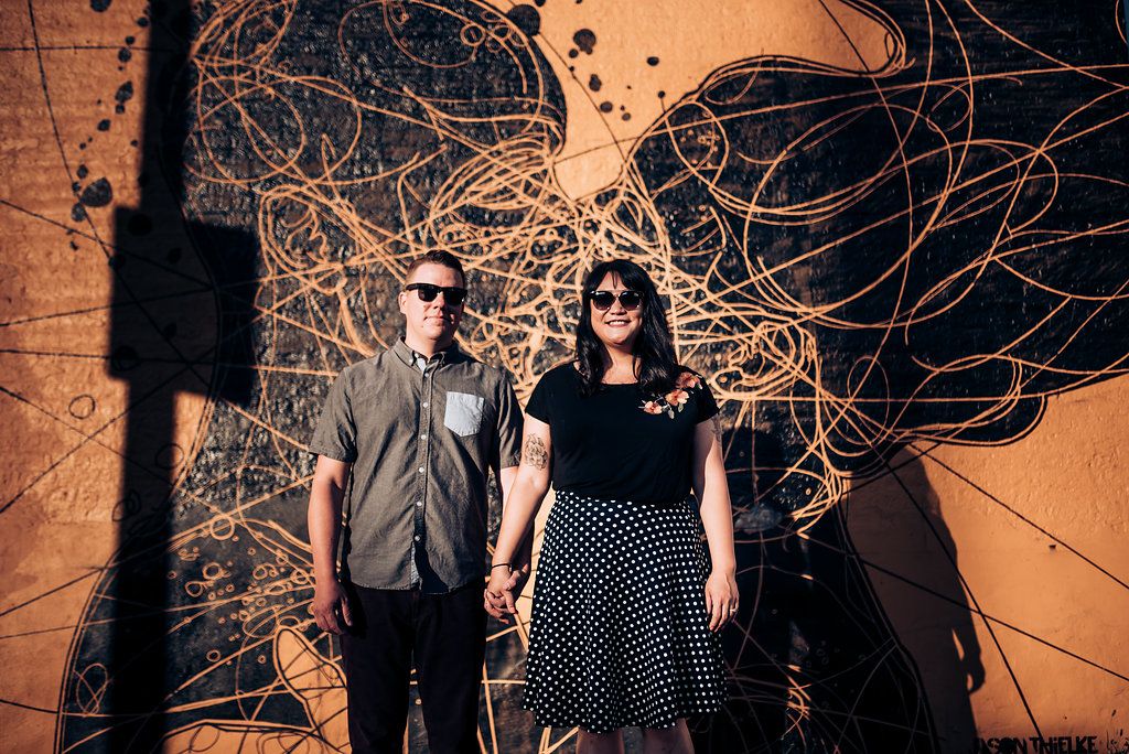 Couple stands against abstract orange wall art in urban setting.