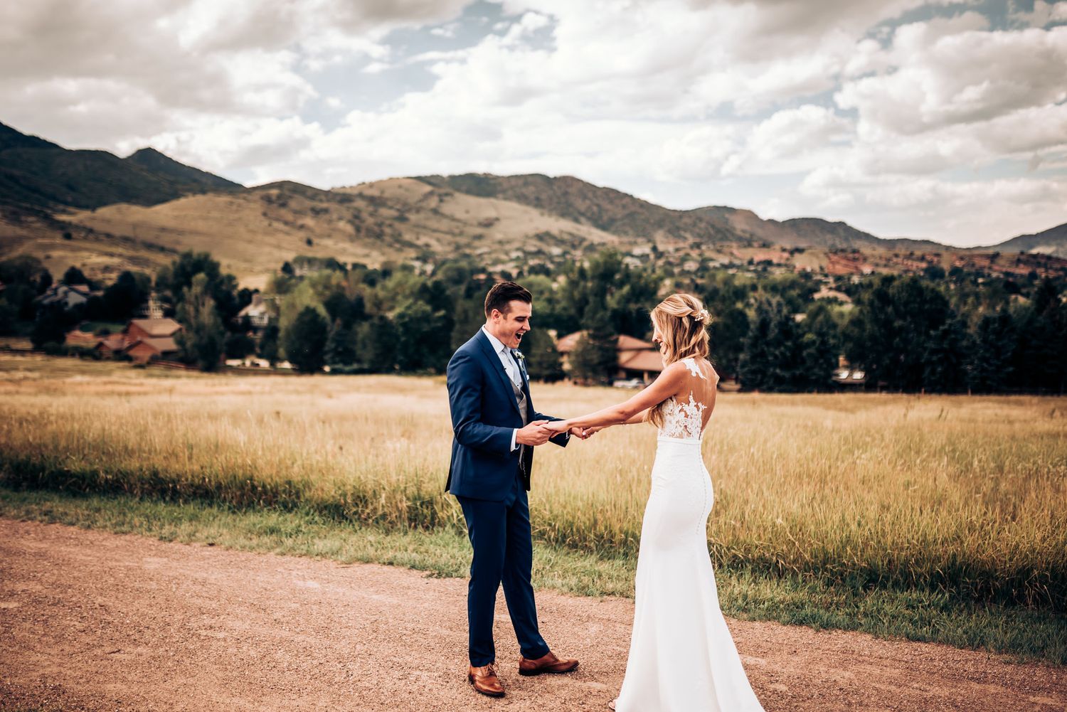 Couple poses on dirt path with scenic mountain backdrop during outdoor wedding photoshoot.