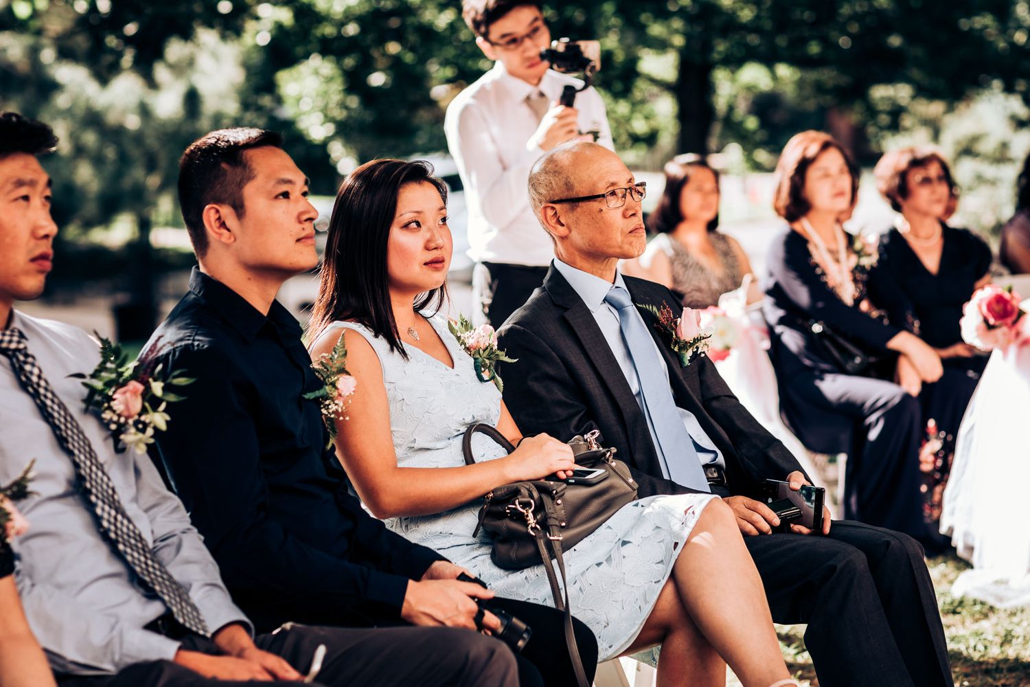 Wedding guests seated outdoors watch the ceremony unfold on a sunny day.