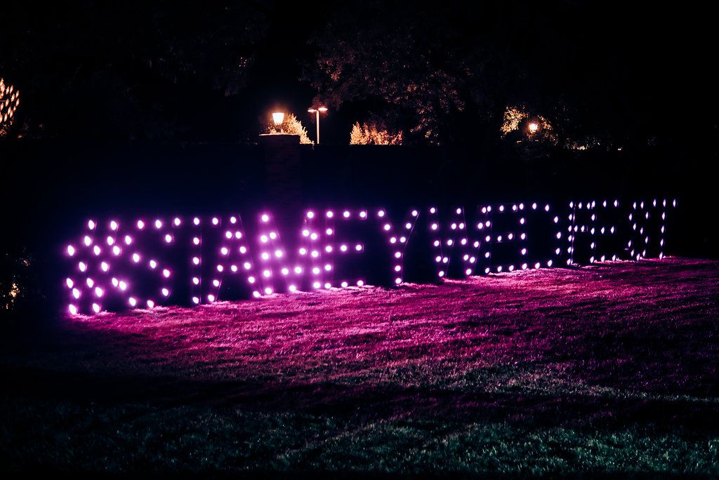 Purple LED lights spelling out text against a dark background in an outdoor setting.