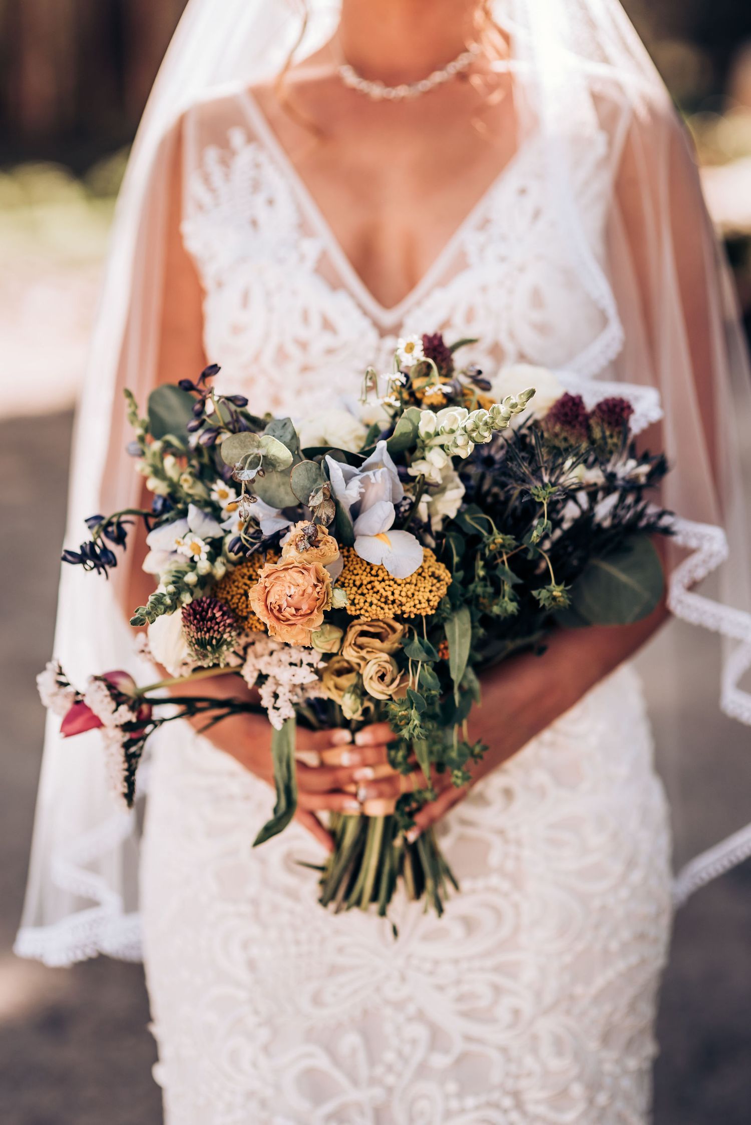 Detailed shot of bridal bouquet with peach roses and greenery against a lace wedding dress.