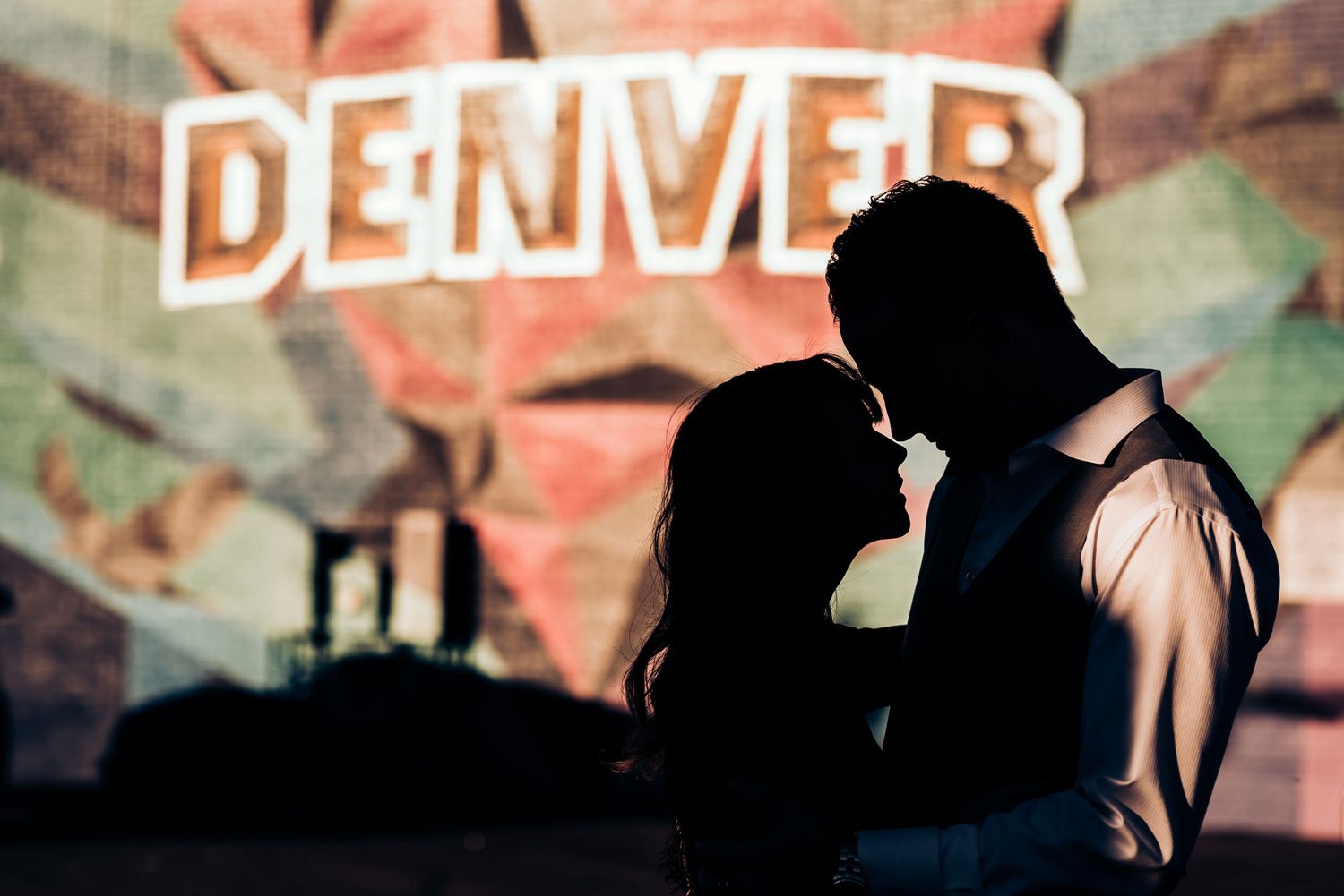 A silhouetted couple poses intimately against a Denver sign backdrop.