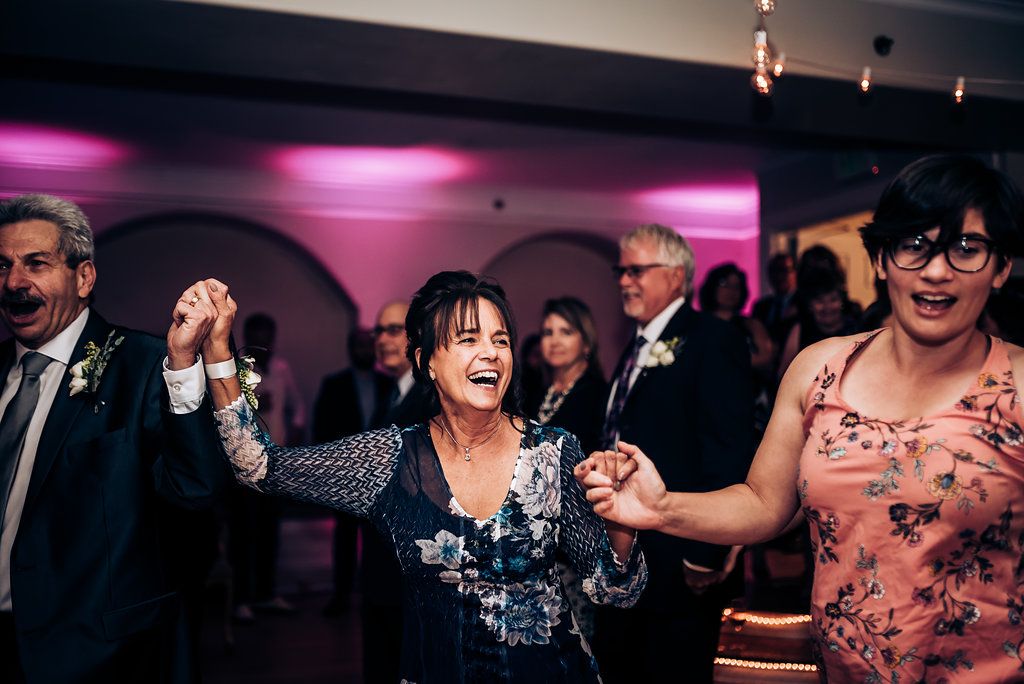 Guests celebrating joyfully on the dance floor at an evening wedding reception with pink ambient lighting.