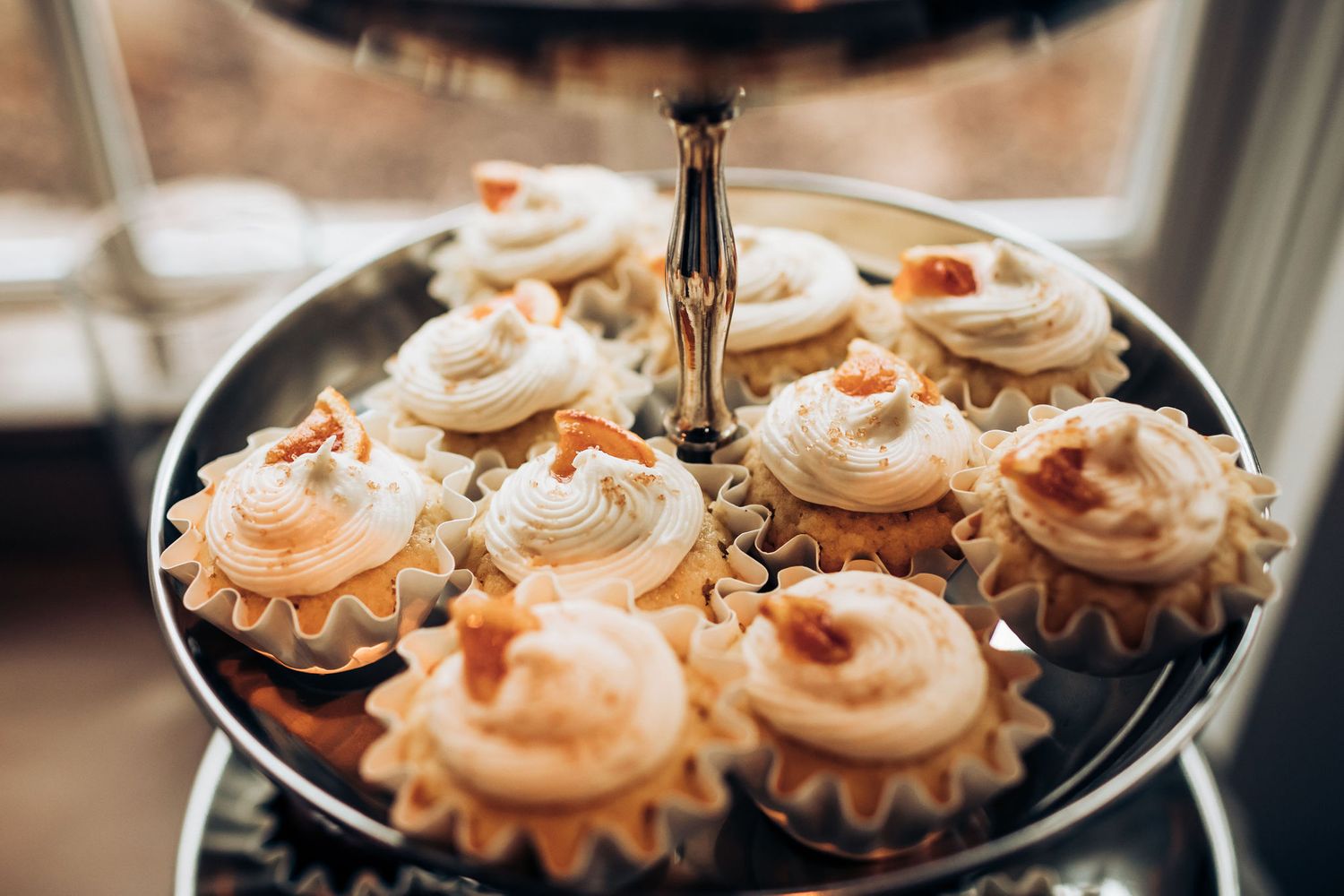Vanilla frosted cupcakes displayed on elegant tiered silver serving stand.