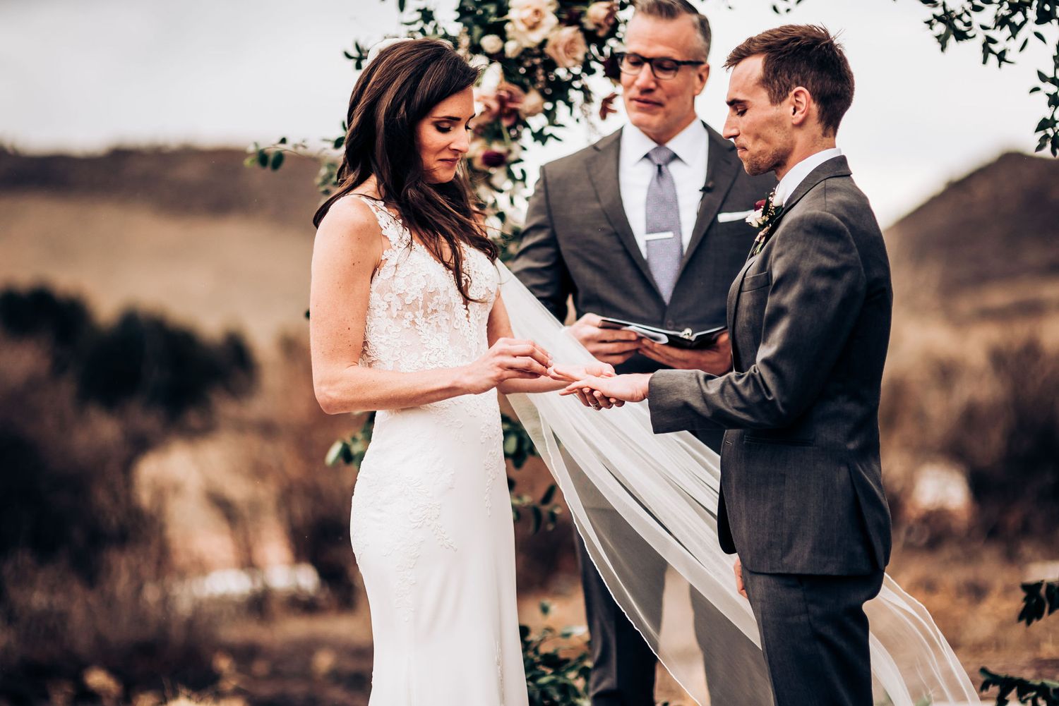 Intimate wedding ceremony moment during ring exchange under floral arch.