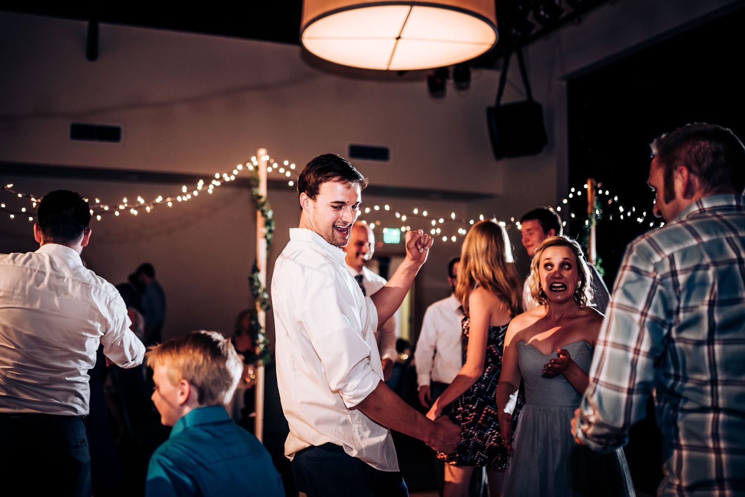 Evening wedding celebration with guests dancing under decorative string lights and pendant lamps.
