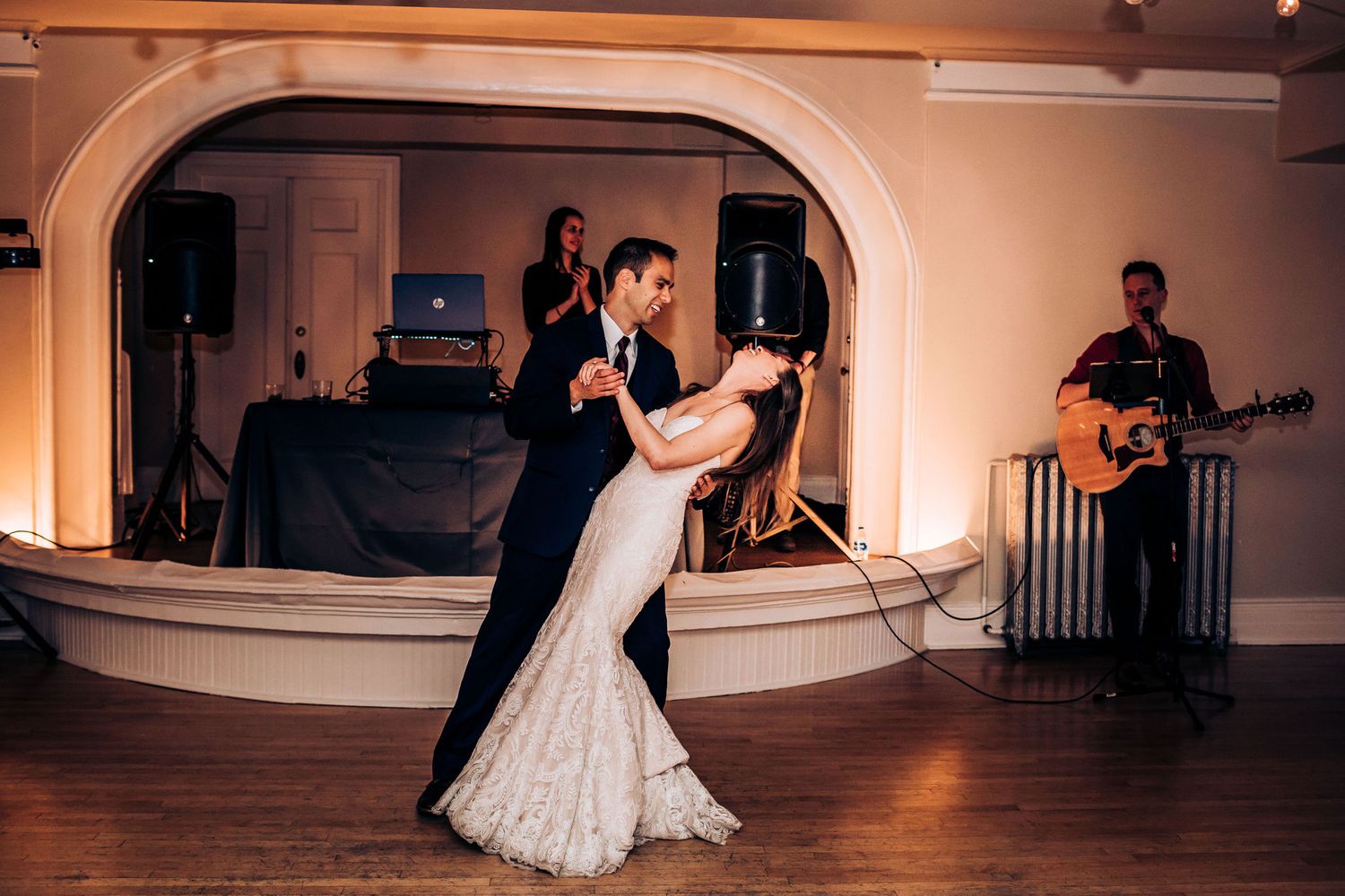 A couple dances on a wooden floor while a guitarist performs in the background.