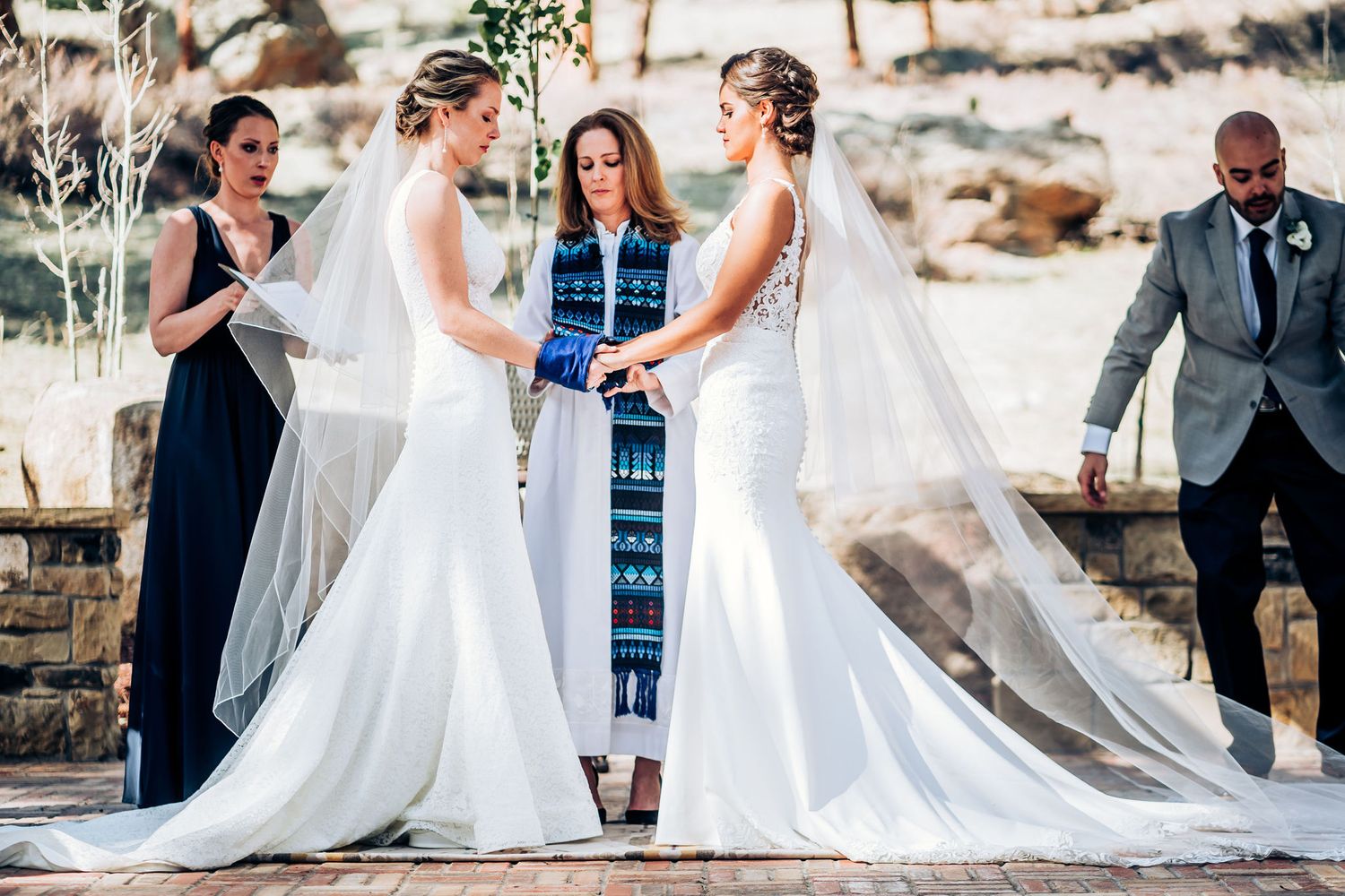 An intimate outdoor wedding ceremony with attendants in navy and an officiant in blue stole.