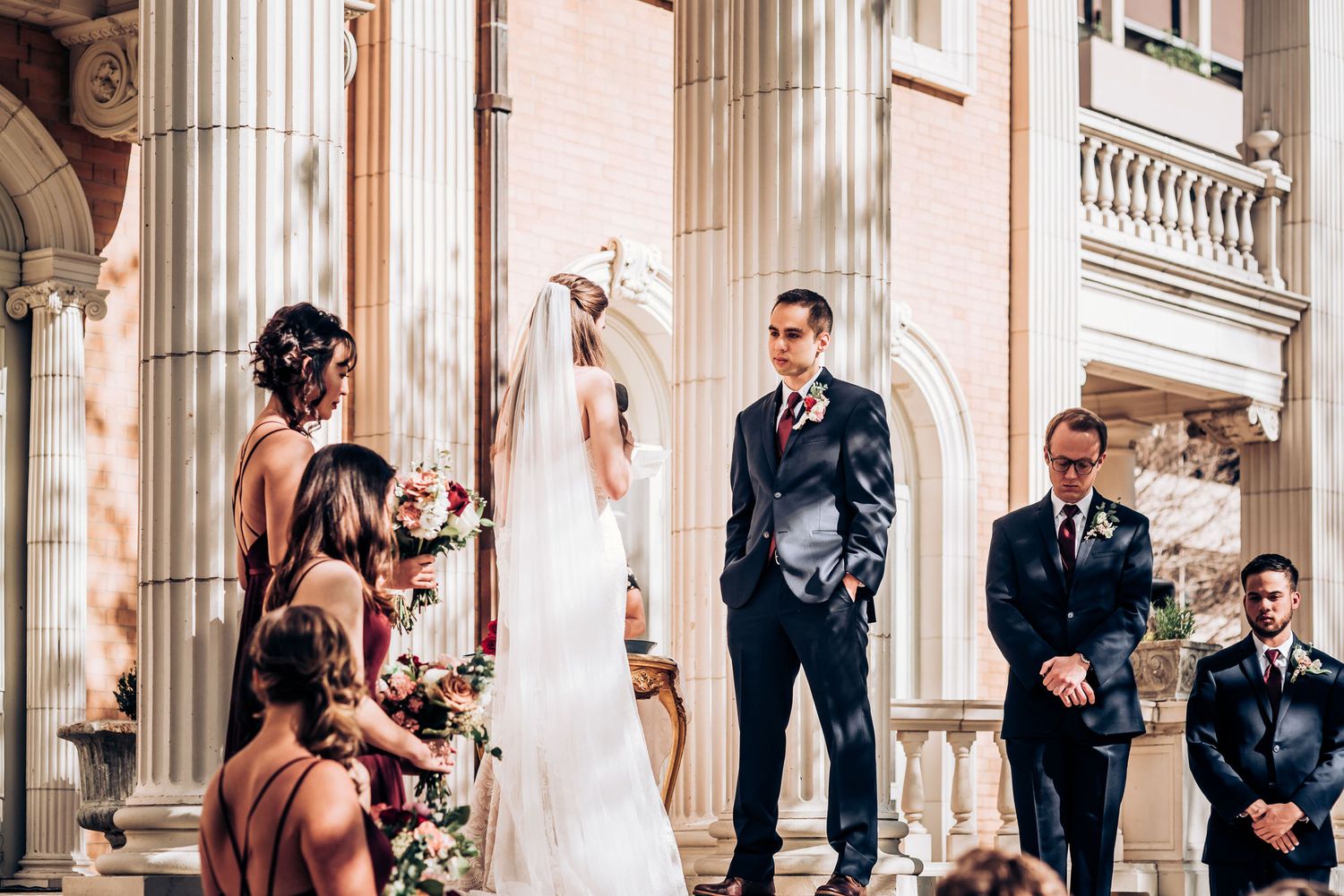 Elegant wedding party gathered on grand stone steps with classical columns during ceremony.