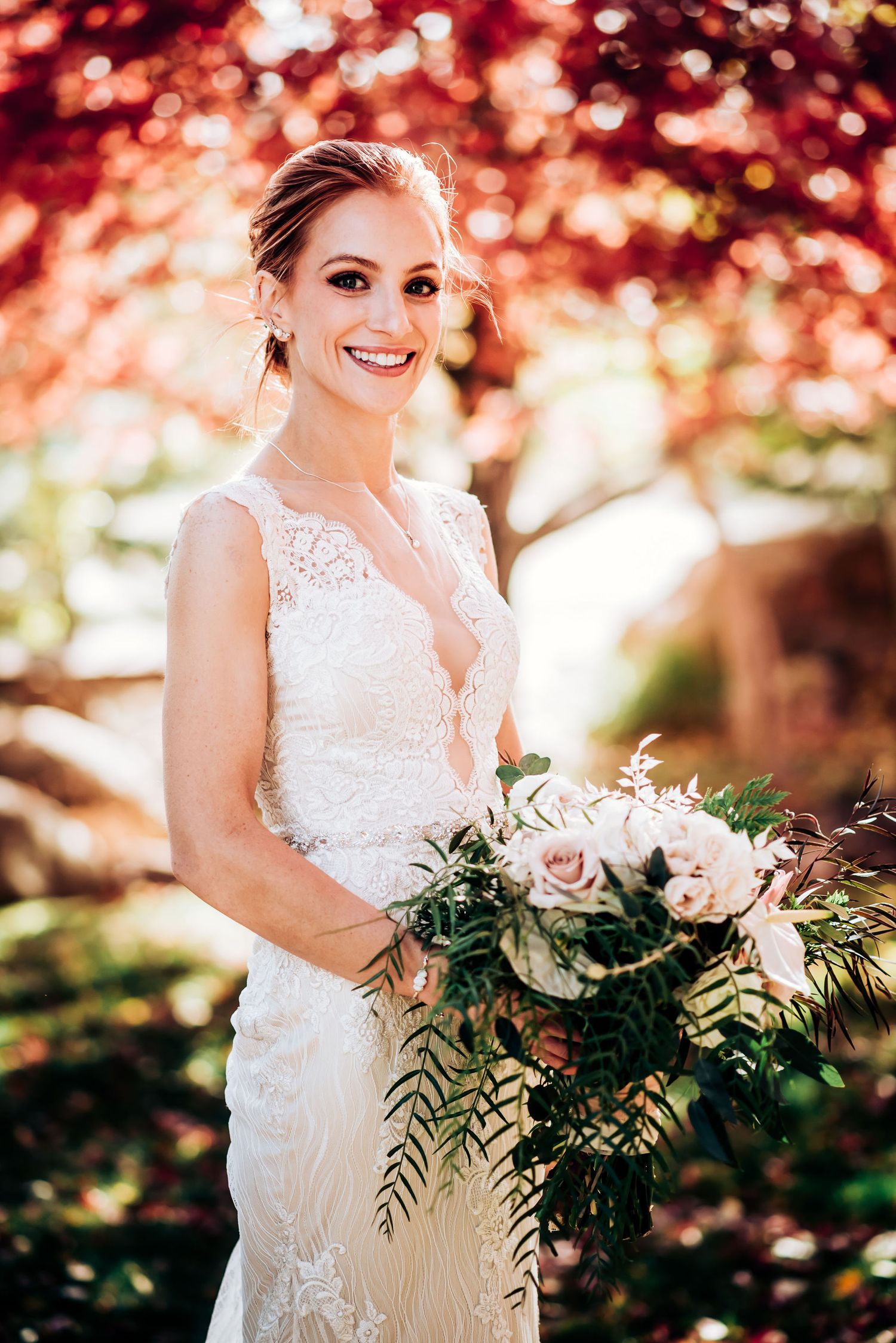 Beautiful wedding dress with delicate lace details and bouquet of pink roses against autumn foliage background.