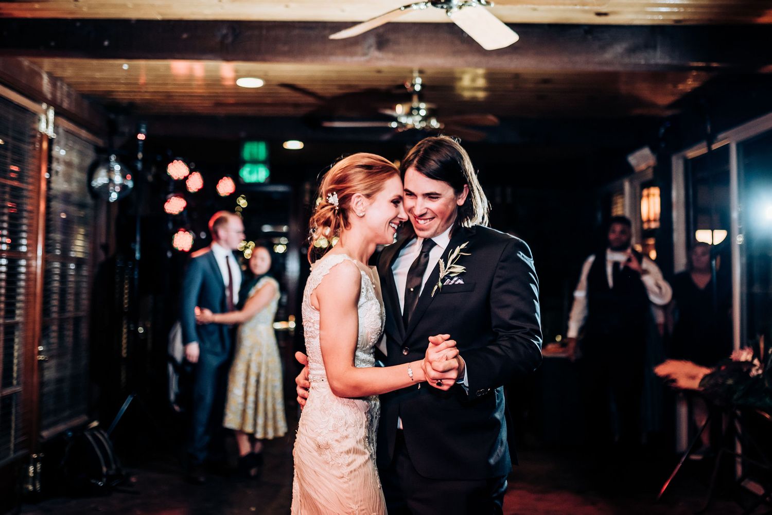 A couple shares a tender moment during their first dance at a dimly lit wedding reception venue.