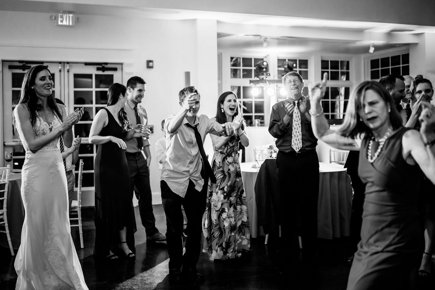 Black and white photo of wedding guests dancing and celebrating at an indoor reception.
