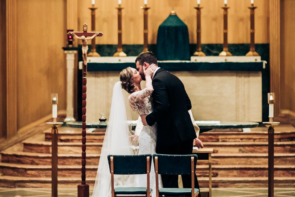 A romantic moment during a church wedding ceremony with lit candles and an altar in the background.