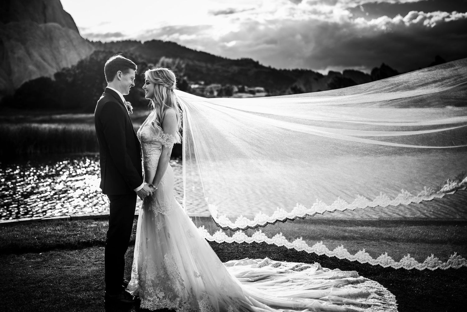 Black and white wedding photograph with dramatic veil movement against mountain landscape.