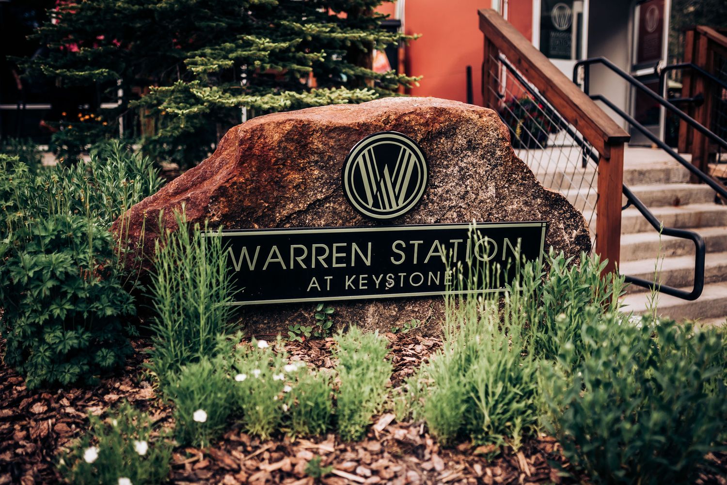 Stone sign for Warren Station at Keystone surrounded by landscaping and evergreen trees.