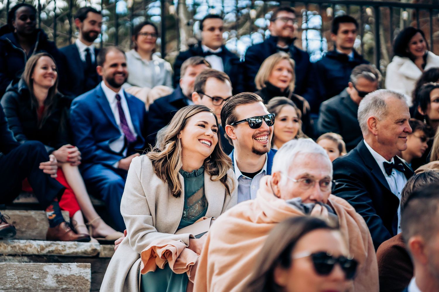 Joyful wedding guests laugh during outdoor ceremony seating.