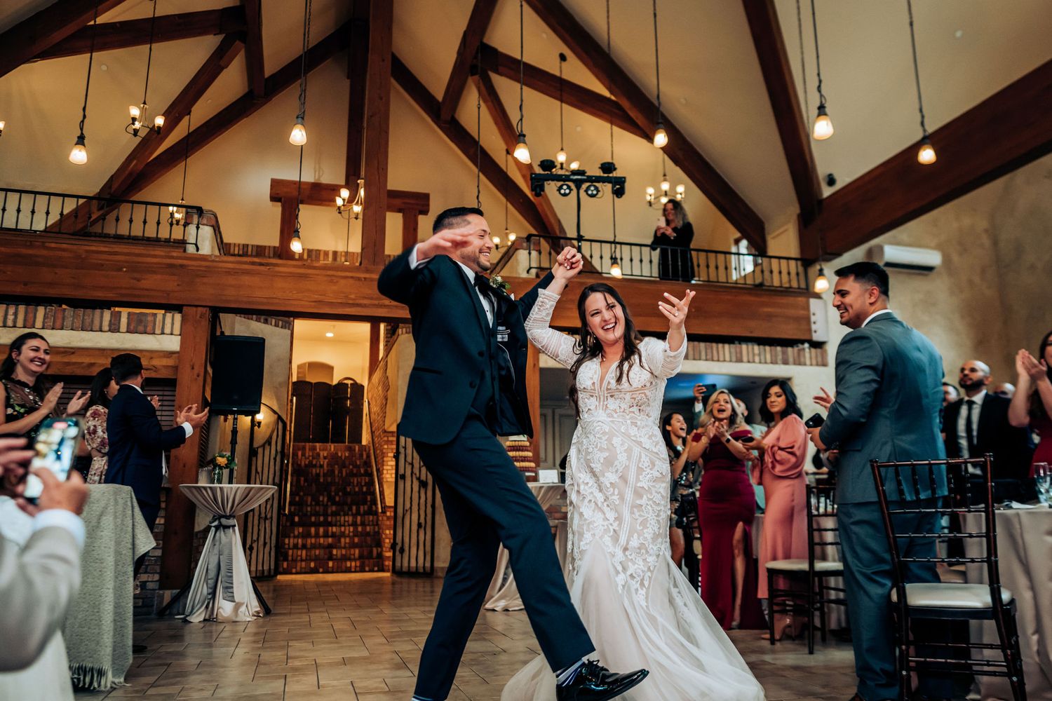 Wedding celebration with dancing guests in a rustic venue with wooden beams and high ceilings.