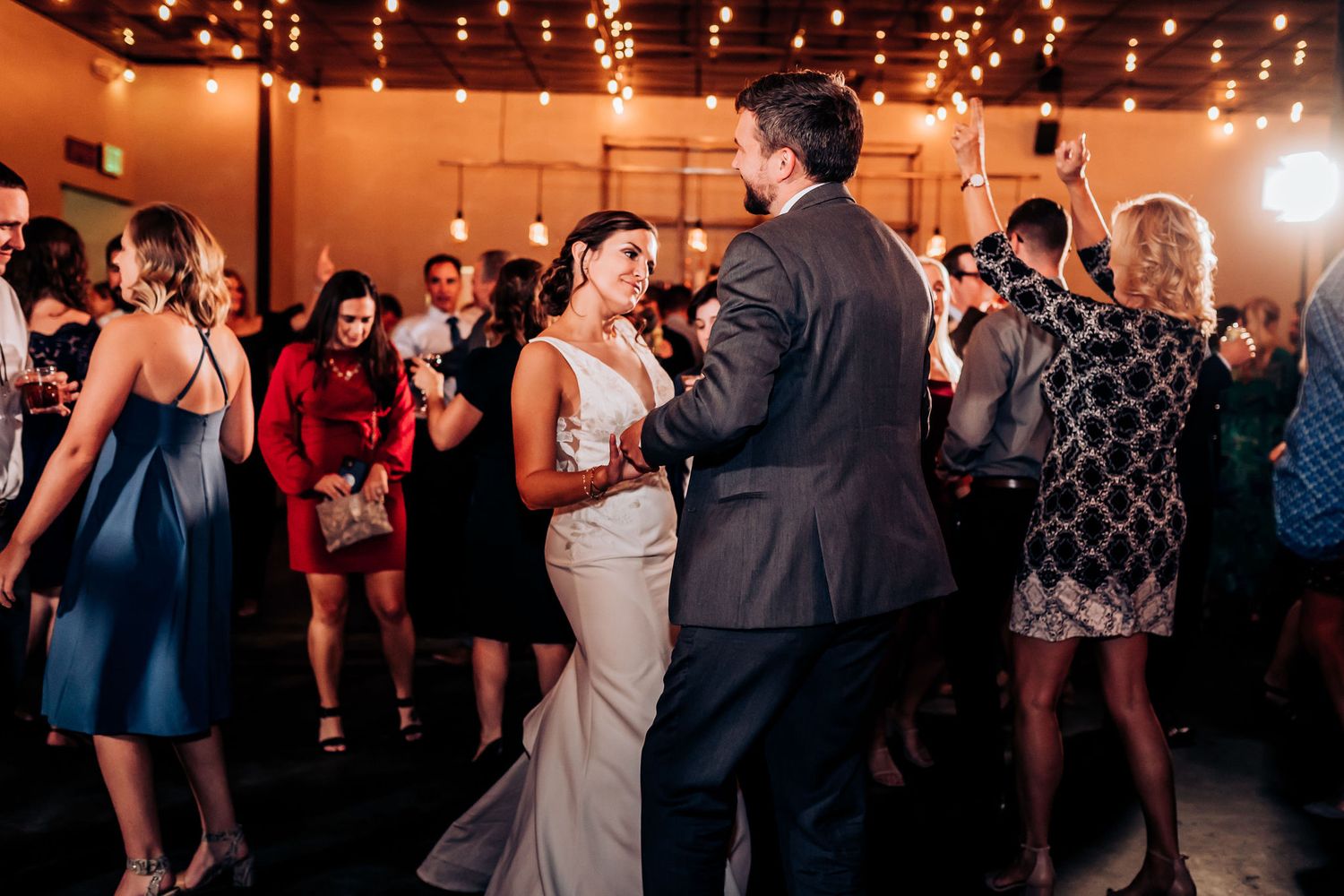 Wedding reception dance floor filled with guests celebrating under warm indoor lighting.