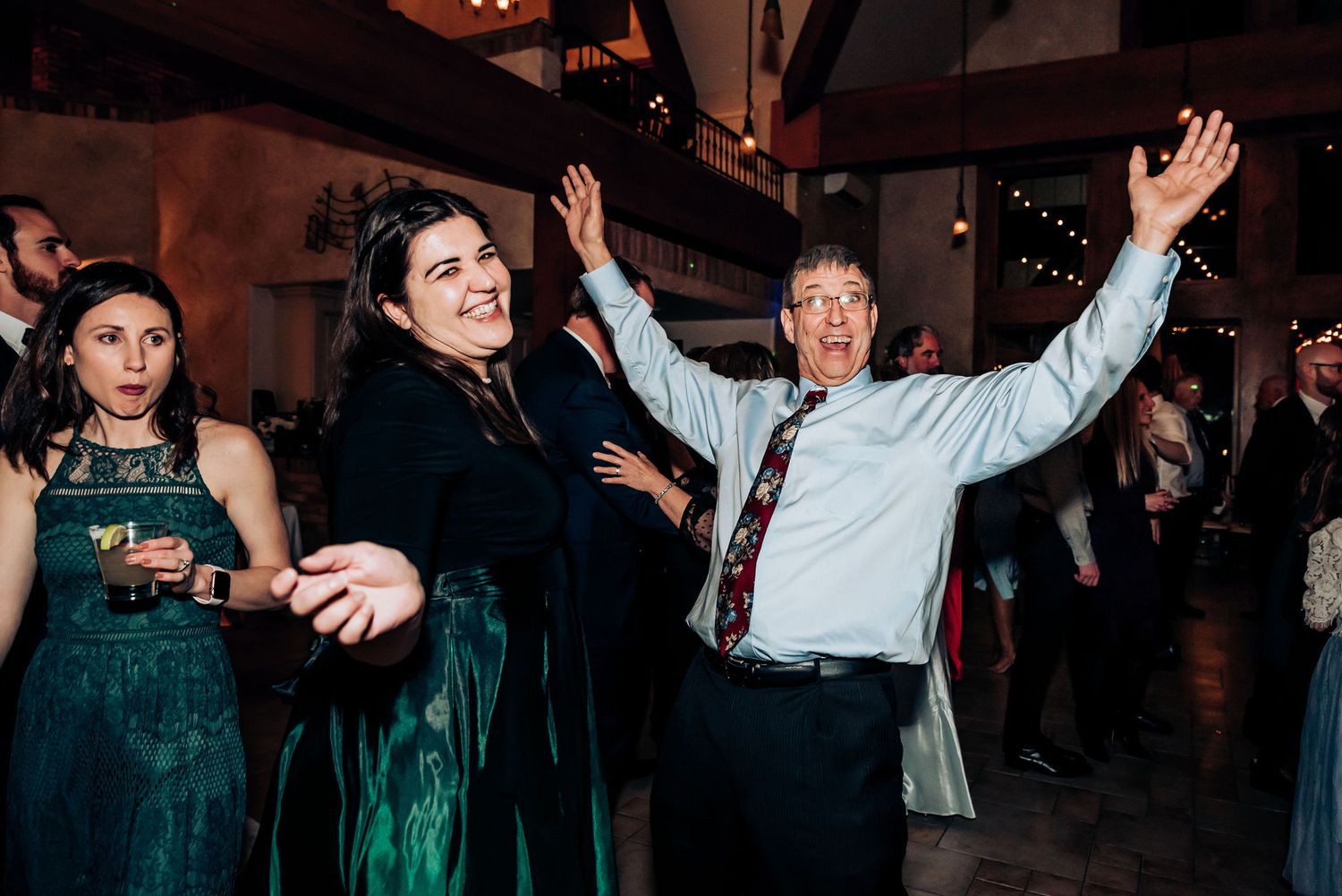 Party guests dancing enthusiastically with raised arms under indoor venue lighting.