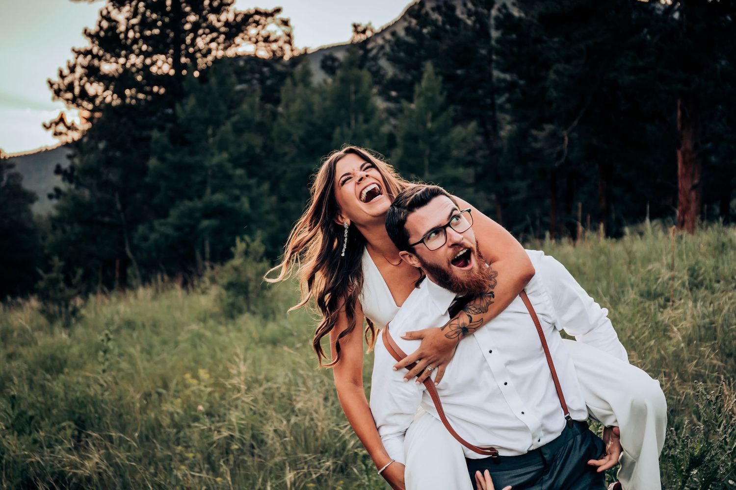 Candid wedding photo showing joyful laughter in a mountain meadow setting.