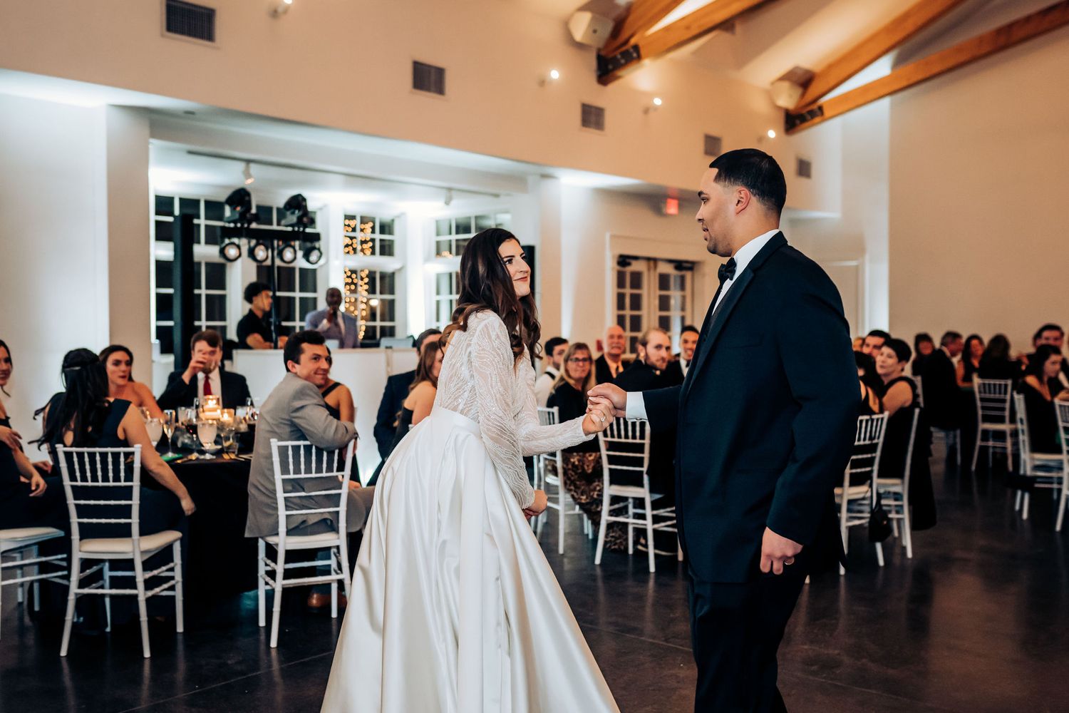Elegant wedding reception with couple at center in venue with wooden beam ceiling.