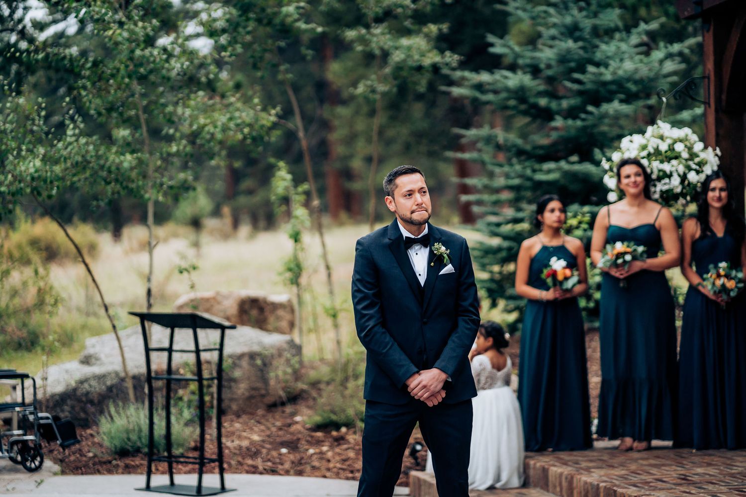 A wedding ceremony at an outdoor venue with bridesmaids in navy dresses and decorative floral arrangements.