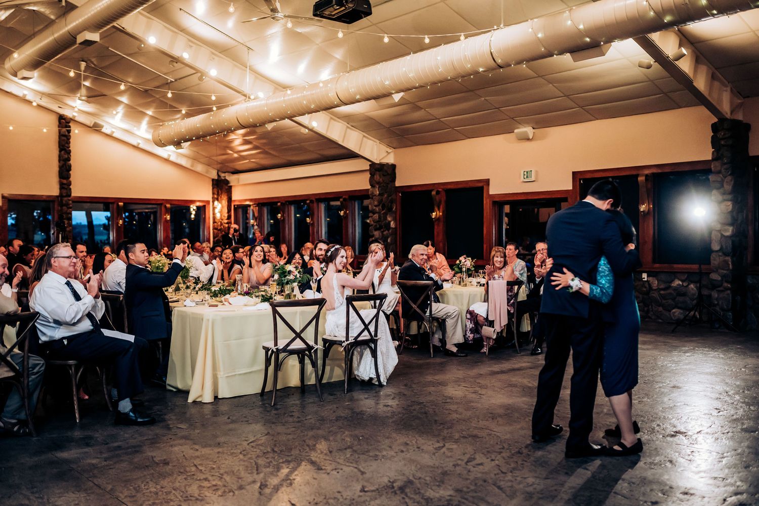 A wedding reception venue with guests seated at tables while a couple dances in the center.