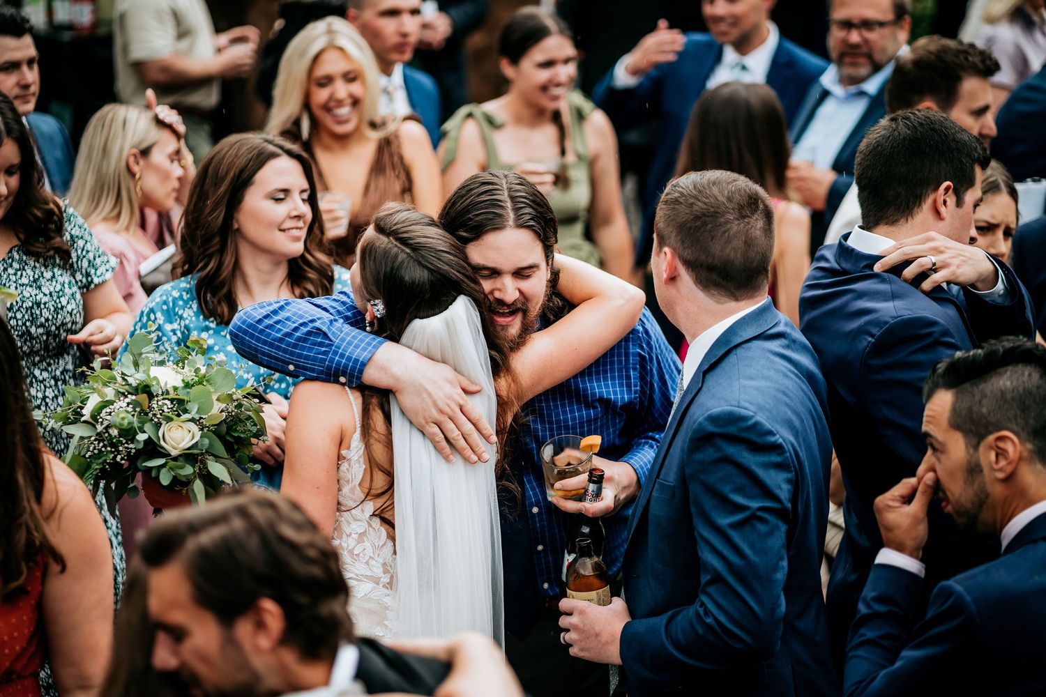 Wedding guests celebrate and embrace during outdoor reception cocktail hour.