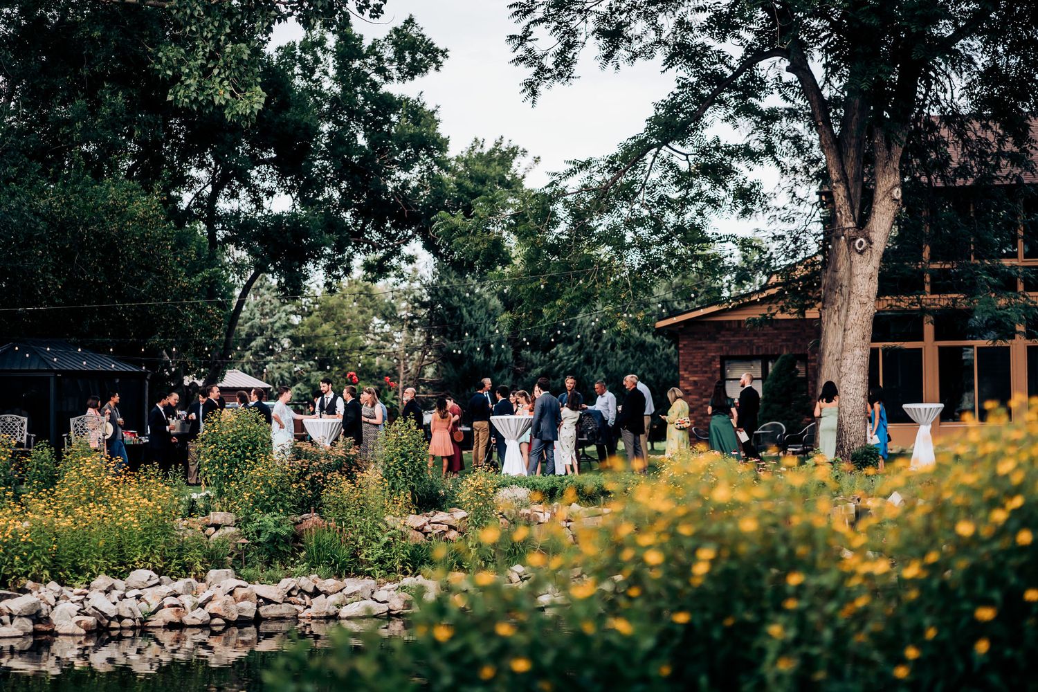Wedding reception venue with yellow wildflowers and rustic wooden buildings in a garden setting.